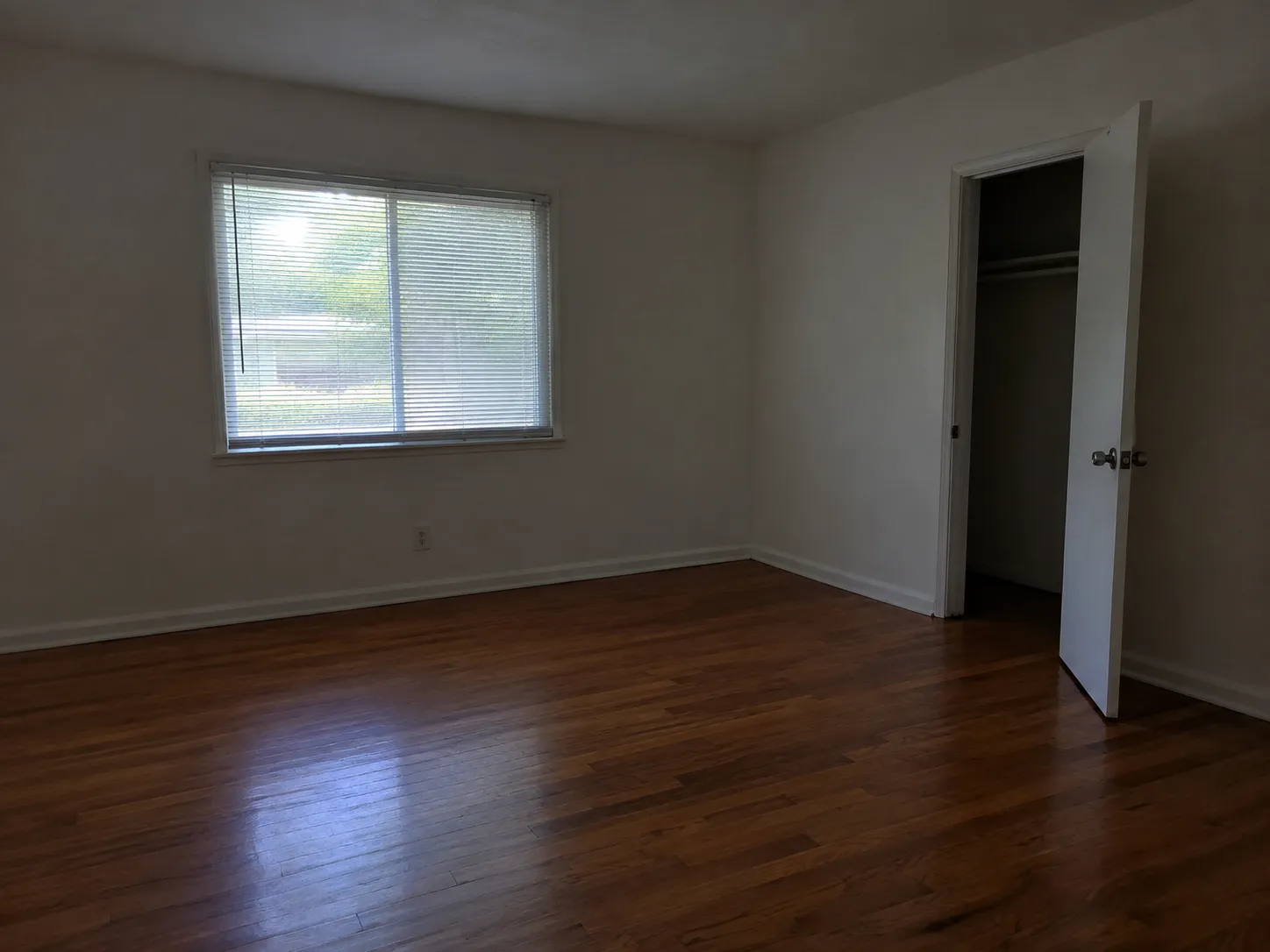 Original photo of the same bedroom, empty with a wood floor and a window